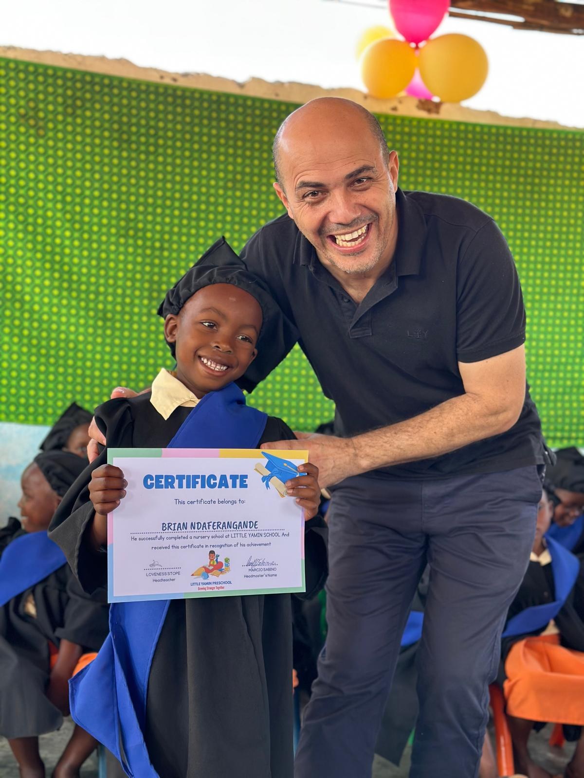 Aluno formando sorrindo ao lado do fundador, segurando seu certificado