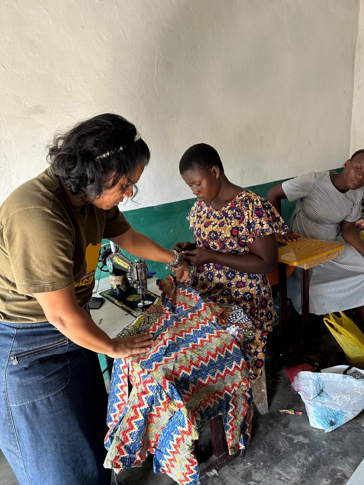 Voluntária ajudando uma viúva a ajustar o tecido na máquina de costura